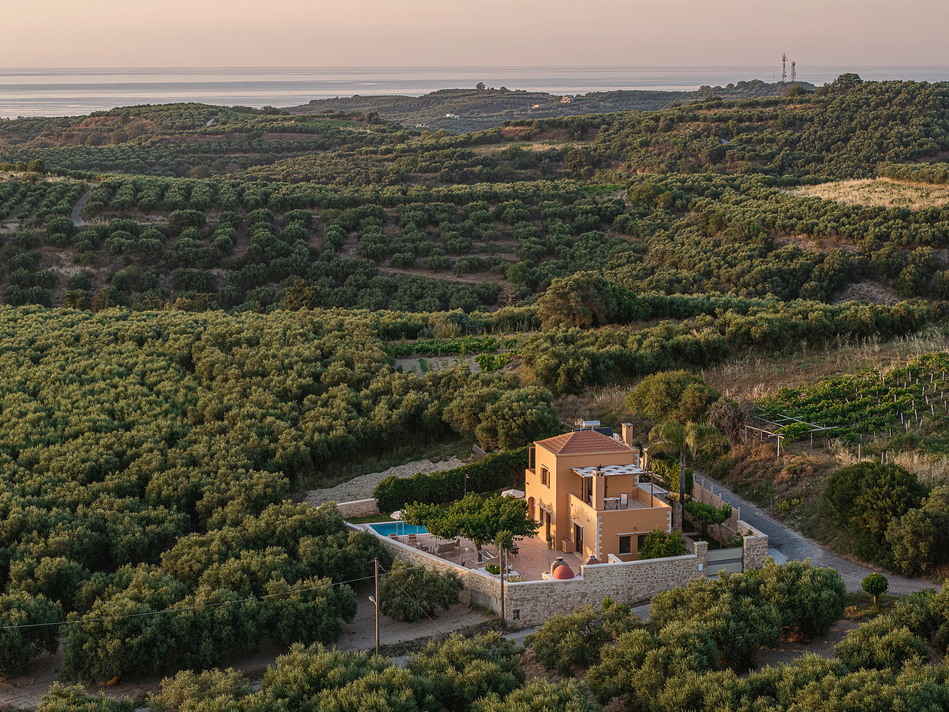 Dusk: the house and its walled garden among the olive groves, the sea at the top of the frame
