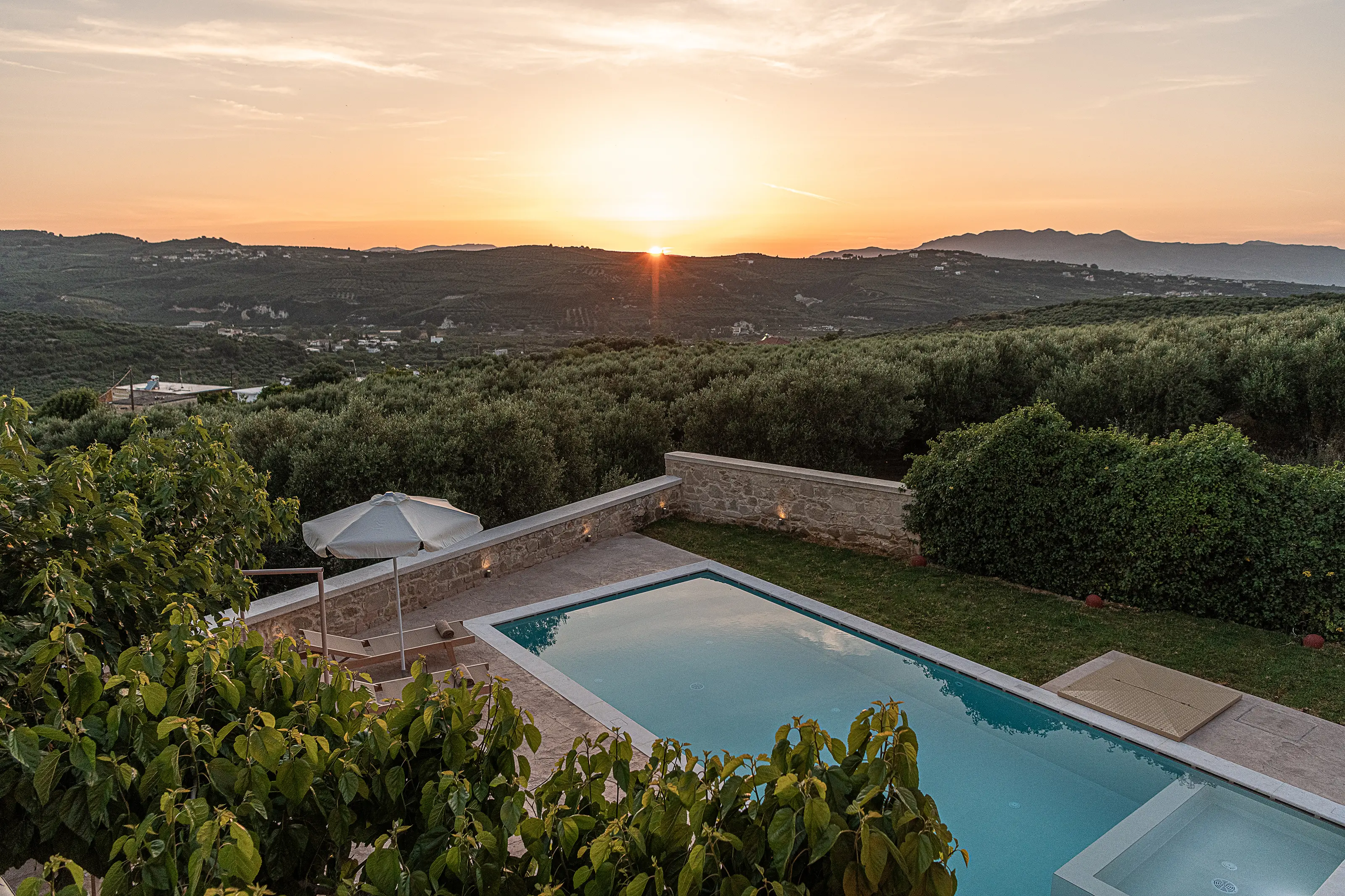 Sunset from the garden: the sun on the ridge, the valley of olive groves below, the lit pool in the foreground